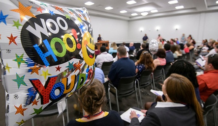 Large room filled with people and a ballon with WooHoo in foreground.